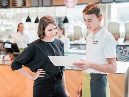 Restaurantmitarbeiter zeigt Dokument einer Kundin.