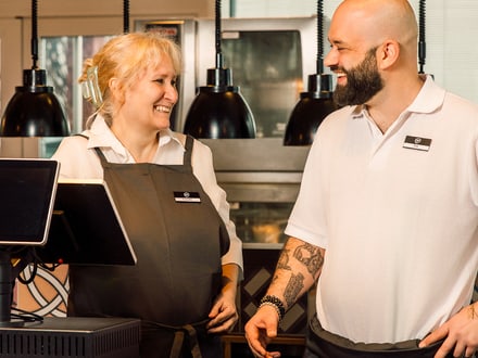 Zwei lächelnde Mitarbeiter im Restaurant hinter der Theke.