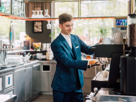 Mann in Anzug bedient Kaffeemaschine in Café.