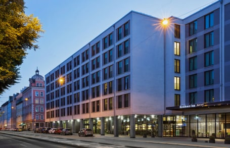 Moderne Hotel-Fassade bei Dämmerung mit beleuchteten Fenstern und geparkten Autos.