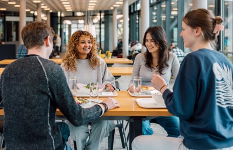 Vier Personen sitzen lächelnd in der Kantine am Tisch."  