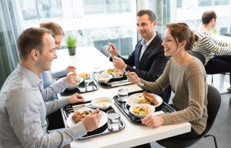 Vier Personen beim Essen an einem Tisch in einem Restaurant mit grossen Fenstern 