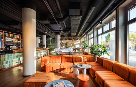 Modernes Café mit orangen Sofas und grossen Fenstern.