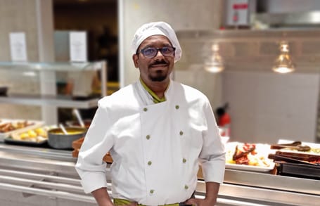 Cuisinier avec lunettes et uniforme blanc dans une cantine.