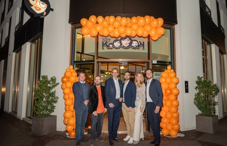 Sechs Menschen vor Hoteleingang mit orangenen Luftballons.",