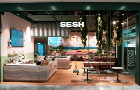 SESH Restaurant mit Leuchtschrift ein paar Bänken und Stühlen einer Schaukel und Bildschirmen und Bestelltresen im Hintergrund