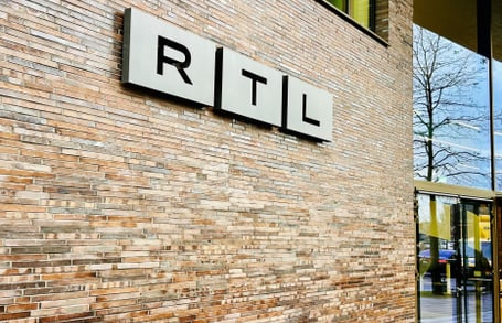 Backsteinwand mit RTL-Logo und Glastür.",