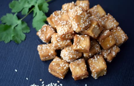 Gebratene Tofuwürfel mit Sesam, Korianderzweig im Hintergrund.