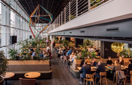 Geschäftsleute in modernem Café mit geometrischem Kunstwerk und Pflanzen.