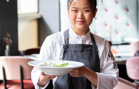Köchin in schwarzer Schürze hält Teller mit Essen im Restaurant.