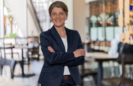 Portrait von Yvonne Wicki, stehend mit verschränkten Armen in einer Hotellobby