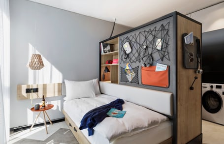 Kleines Schlafzimmer mit Bett, Trennwand und Waschmaschine.