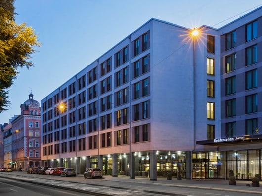 Moderne Hotel-Fassade bei Dämmerung mit beleuchteten Fenstern und geparkten Autos.