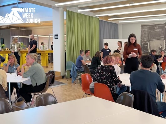 Menschen sitzen an Tischen bei Veranstaltung 'Climate Week Zurich'.