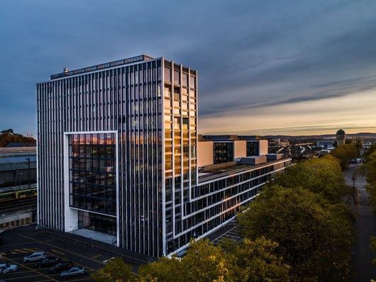 Hochhaus bei Sonnenuntergang mit Bäumen und Autos.