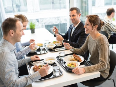 Vier Personen beim Essen an einem Tisch in einem Restaurant mit grossen Fenstern 