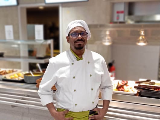 Cuisinier avec lunettes et uniforme blanc dans une cantine.