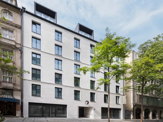 Moderne Mehrfamilienhausfassade mit Bäumen davor.