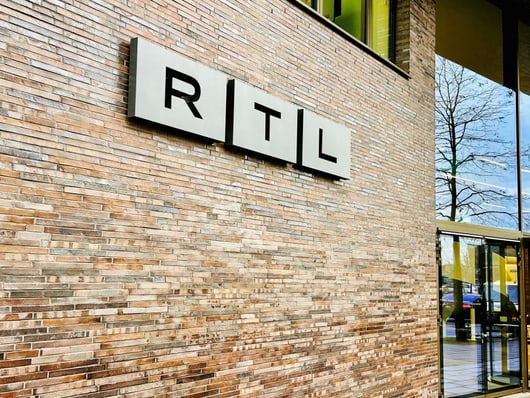 Backsteinwand mit RTL-Logo und Glastür.",