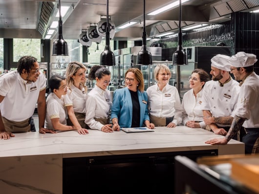 Gruppe von Köchen und Servicepersonal bespricht Pläne in einer Restaurantküche.