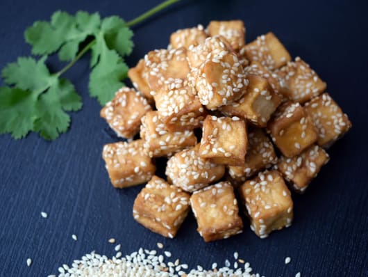 Gebratene Tofuwürfel mit Sesam, Korianderzweig im Hintergrund.