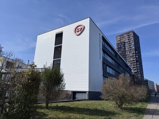 Bürogebäude mit SV-Logo, blauem Himmel, grüner Umgebung.
