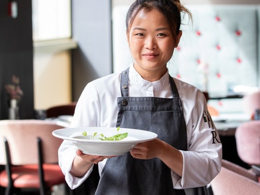Köchin in schwarzer Schürze hält Teller mit Essen im Restaurant.