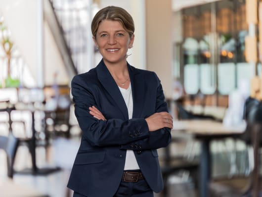 Portrait von Yvonne Wicki, stehend mit verschränkten Armen in einer Hotellobby