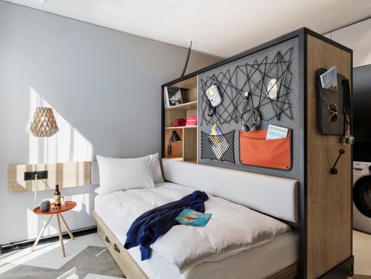 Kleines Schlafzimmer mit Bett, Trennwand und Waschmaschine.