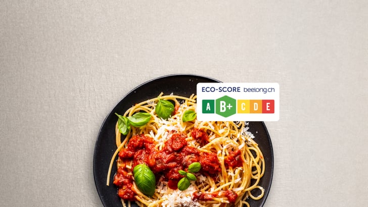 Spaghetti mit Tomatensauce, Basilikum und geriebenem Käse auf schwarzem Teller, Eco-Score Label.