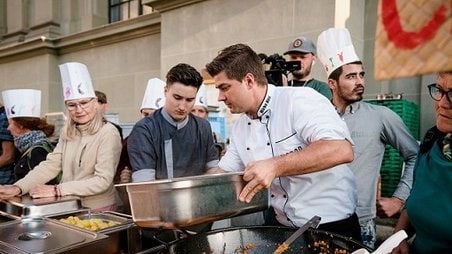 Kochkurs im Freien mit Chefkoch und Teilnehmern, die Paella zubereiten.
