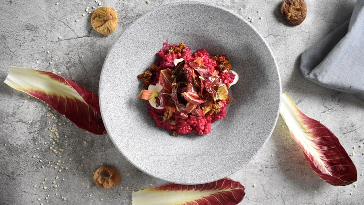 Grauer Teller mit buntem Gericht, umgeben von Radicchio und getrockneten Feigen.