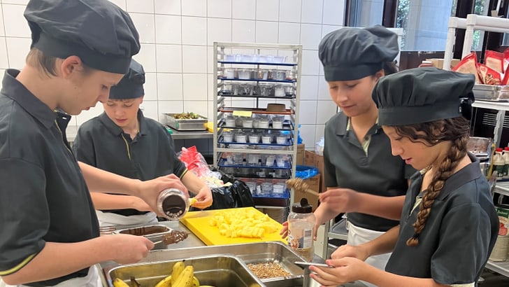 Kinder in einer Küche, die Bananen und Trauben zubereiten, tragen Kochmützen.