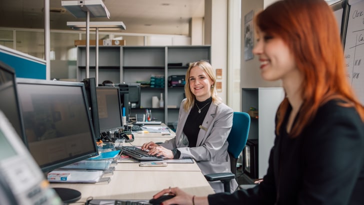 Zwei Frauen arbeiten lächelnd an Computern im Büro.