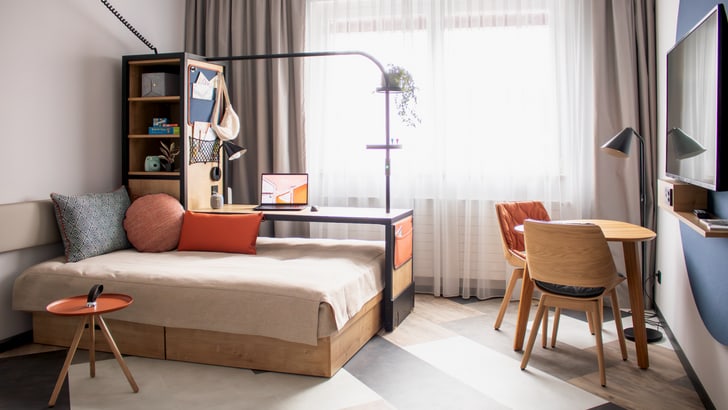 Modern eingerichtetes Hotelzimmer mit Bett, Schreibtisch und hellem Fenster.