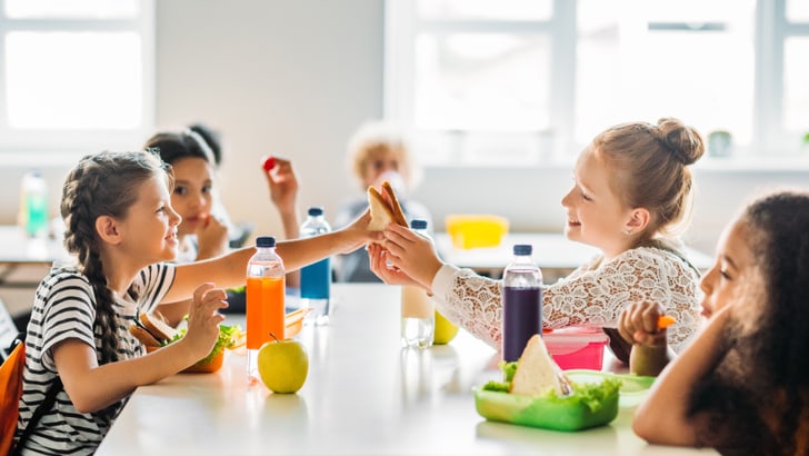 Kinder beim Essen und Händeschütteln in der Schulcafeteria.