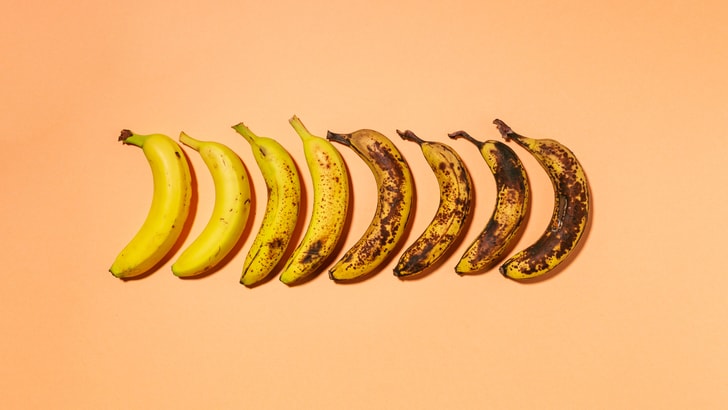 Acht Bananen in verschiedenen Reifestadien auf orangefarbenem Hintergrund.