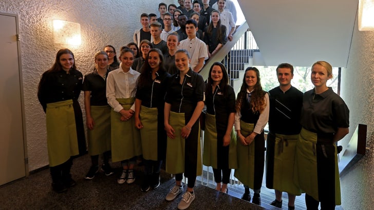 Gruppe von jungen Restaurantmitarbeitern mit Schürzen auf einer Treppe.