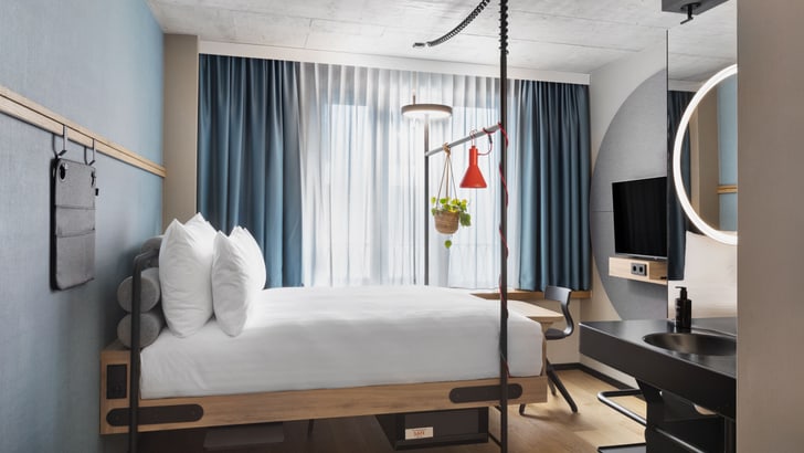 Modernes Hotelzimmer mit grossem Bett und Schreibtisch unter dem Fenster.