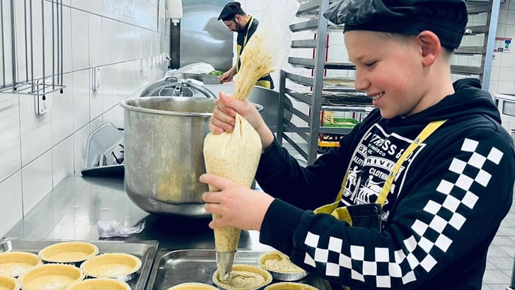 Kind füllt Teig in Backformen in Bäckerei.