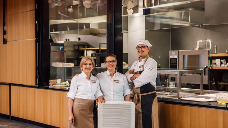 Drei Restaurantmitarbeiter lächelnd vor einer Küche.