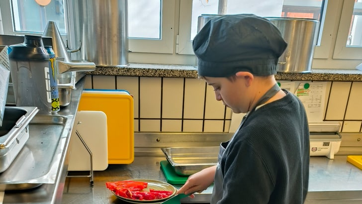Kind schneidet Paprika in der Küche mit Tabletts auf dem Tisch.