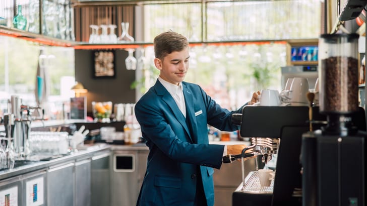 Mann in Anzug bedient Kaffeemaschine in Café.