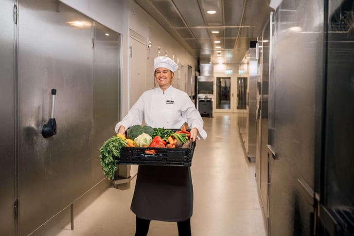 Koch in Küche mit Kiste voller Gemüse.