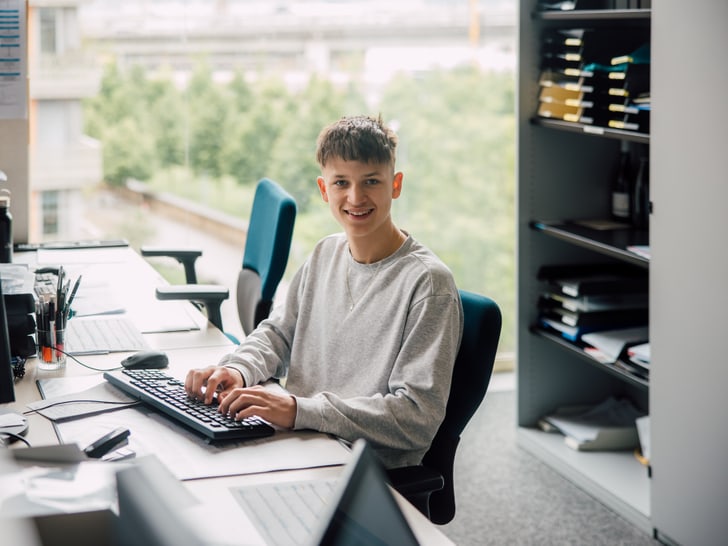Junger Mann sitzt am Schreibtisch mit Computern im Büro.