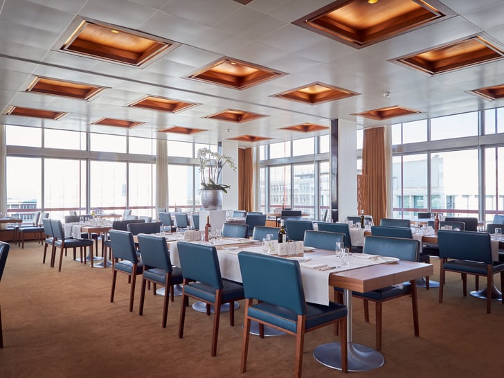 Modernes Restaurant mit blauen Stühlen und Tischen, grosse Fenster.