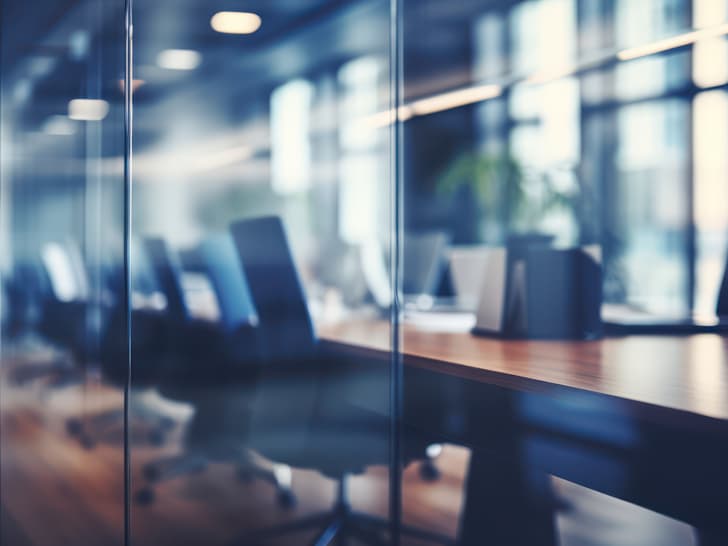 Moderne Büroinnenansicht durch Glas mit reflektierenden Oberflächen und Computerarbeitsplätzen.