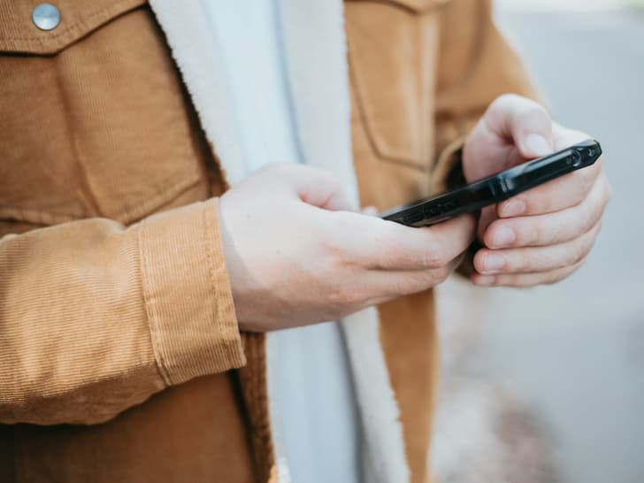 Person in brauner Jacke hält ein Smartphone.