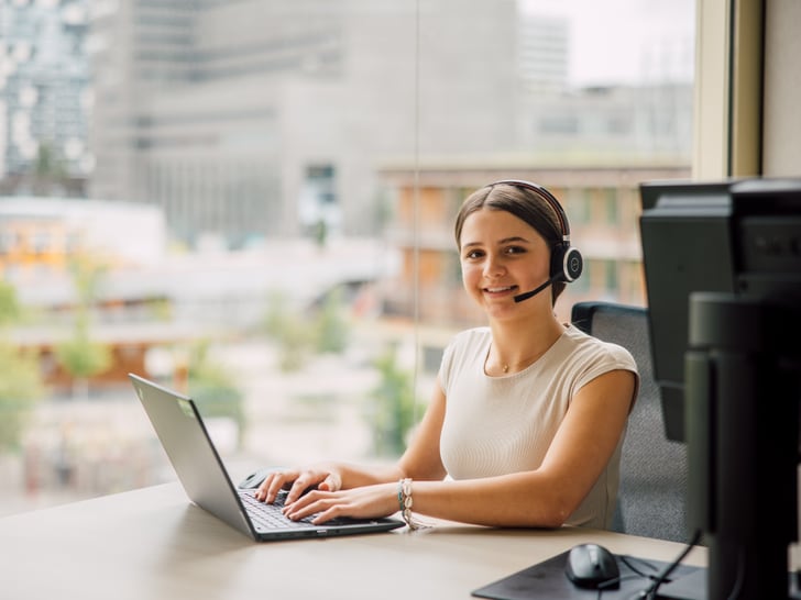 Frau mit Headset arbeitet am Laptop im Büro.