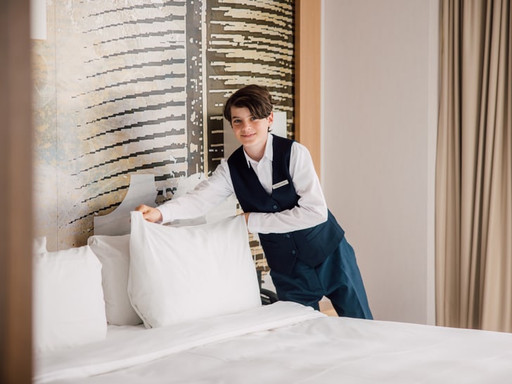 Lernender Hotel richtet Kissen auf Bett vor Wandkunstwerk aus.
